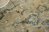 Distressed Tabriz carpet showing intricate floral motifs in sand, faded indigo, and charcoal.