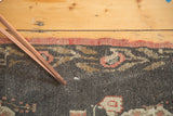 Hand-knotted vintage Oushak rug detail, charcoal field with dark blush floral and cinnabar edge.