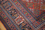 Distressed vintage Joshegan carpet corner with rich brick red and navy patterned borders.