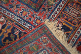 Corner detail of vintage Joshegan rug, featuring fine brick red, navy, gold patterns and ivory fringe.