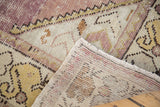 Corner of distressed Oushak runner showing hand-knotted backing, muted purple and gold patterns.