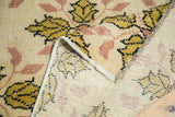 Detail of a folded vintage Oushak rug, revealing hand-knotted foundation and saffron, blush floral pile.
