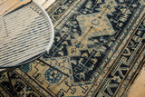 Distressed Malayer rug featuring intricate navy geometric patterns, beige field, and visible edge wear.