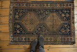 Distressed Qashqai rug corner with tattered edge, navy field, and copper geometric patterns.