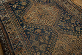 Distressed Qashqai rug with dark indigo blue field, stylized tribal motifs, and visible worn texture.