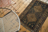 Distressed Qashqai rug's geometric border, tattered edge, and deep indigo field with floral motifs.