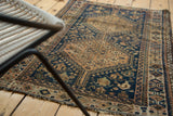 Tattered fringe and geometric border of a distressed Qashqai rug corner in copper and navy.
