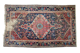 Distressed antique Josan Sarouk rug with geometric diamond medallion, rich navy, madder red, and visible textural wear.