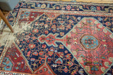 Distressed navy blue antique Josan Sarouk rug with exposed foundation and geometric red-pink patterns.