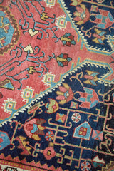 Distressed antique Josan Sarouk rug showing geometric vinery in grapefruit red and navy fields.