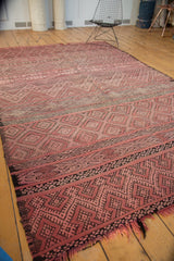 Intricate banded dusty rose and charcoal geometric patterns on vintage Moroccan Jijim rug end, with frayed fringe.