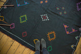 Embroidered fuchsia, saffron, aqua, and green geometric motifs on black Kilim carpet.