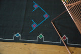 Embroidered geometric diamond patterns in aqua, green, and fuchsia on a black Kilim rug.