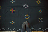 Jet black Moroccan kilim with aqua, green, yellow, red embroidered diamond motifs.