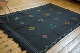 Black Moroccan Kilim carpet featuring embroidered diamond elements and white zig-zag border.