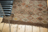 Fringed corner of vintage Turkish Jijim rug with geometric diamonds in brown, ivory, blush, and tangerine.