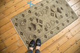 Distressed vintage Oushak rug with muted beige field and dark brown geometric ram's horn motifs.