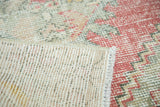 Distressed Oushak runner, its folded corner revealing hand-knotted foundation and worn blush pile.