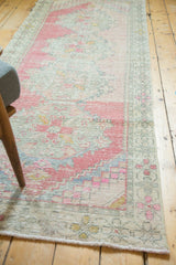 Corner of distressed Oushak runner, with blush pink, seafoam, and gold geometric border.