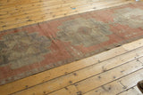 Distressed vintage Oushak runner with a pale cinnabar red field and scalloped medallion.