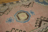 Textured blush field of a distressed vintage Oushak rug, showing blue and brown geometric motifs.