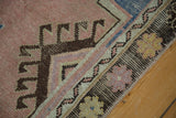 Decorative distressed Oushak rug showing blush, charcoal geometric motifs, and visible foundation.