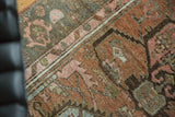 Distressed vintage Malayer rug detail with textured copper pile and blush, teal geometric patterns.