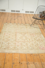 Faded ivory and blush geometric motifs on distressed Oushak rug's secured end and fringe.