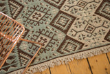 Close-up of a vintage Moroccan Kilim's dusty mint green, dark brown, ivory gul motifs, and fringe.