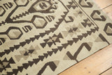 Distressed Kilim rug corner with geometric charcoal, silver, and ivory pattern.