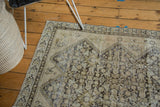 Distressed antique Malayer rug's worn henna plant motifs, beige tones, and exposed foundation.