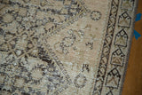 Distressed antique Malayer rug with faded lattice motif, beige tones, and exposed foundation.