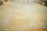 Distressed antique Oushak carpet, displaying faded ivory, gold, and blush patterns with fringe.