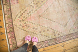 Distressed Khotan runner, blush pink and sand tones, geometric border, and visible knot heads.