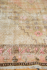 Distressed Khotan rug texture with stepped brown patterns, blush floral motifs, and visible fringe.