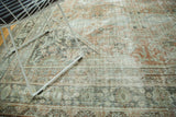 Distressed texture of a vintage Mahal rug, featuring terra cotta, pale sage, and charcoal patterns.