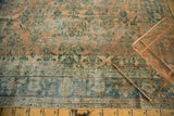 Distressed antique Lilihan carpet with blush and teal potted plant motifs and border.