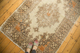 Textured distressed Oushak rug corner showing rectilinear patterns, ivory field, and tangerine spandrel.