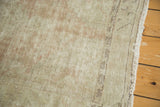 Distressed Oushak rug close-up showing worn pile, pale blush field, serrated border, and fringe.