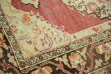 Textured distressed pile on vintage Oushak carpet corner with faded cherry red and coffee brown geometric borders.