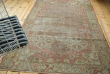 Distressed Oushak rug corner with blush starburst and muted trellis motifs.
