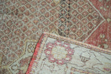 Distressed Oushak rug corner, revealing secured edge, ivory foundation, and worn pile with blush, saffron.