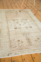 Distressed Oushak rug corner showing worn beige pile, natural fringe, and chocolate brown motifs.