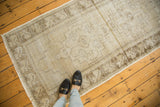 Distressed vintage Oushak rug runner featuring faded beige pile, charcoal brown blossomed flower border, and fringe.