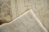 Distressed Oushak rug corner revealing hand-knotted back, fringe, and faded beige pile.