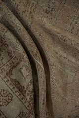 Textured pile of folded distressed Oushak rug, showing mostly even wear and subtle geometric patterns.