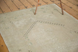 Distressed Oushak rug corner with faded geometric motifs in muted beige and pale green.