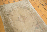 Worn edge of a distressed Oushak rug, displaying faded blush and pale sand floral motifs.