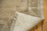 Distressed vintage Oushak rug corner reveals muted beige pile, hand-knotted ivory foundation, and fringe.