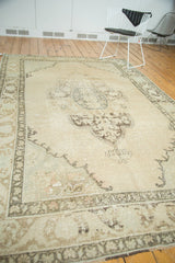 Distressed Oushak rug with faded pale beige field, scalloped medallion, and ornate border.